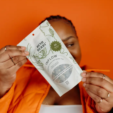 Person holding a 'Bless Berry' product against an orange background