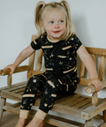 Child wearing a black outfit with white patterns sitting on a wooden bench.