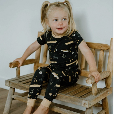Child wearing a black outfit with white patterns sitting on a wooden bench.