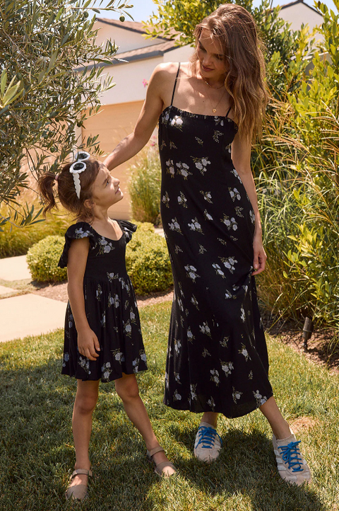 Mother and daughter wearing matching black floral dresses standing outdoors.