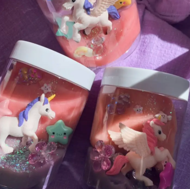 Decorative jars with unicorn figurines and glittery contents on a purple surface