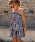 Young girl in a floral dress standing in front of a stone wall with water features.