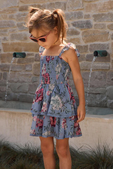 Young girl in a floral dress standing in front of a stone wall with water features.