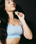 Woman in a blue sports bra holding a vape device against a dark background