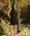 Woman in a black dress standing in a garden with palm trees and rocks.
