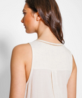 Woman wearing a light-colored sleeveless top against a plain background