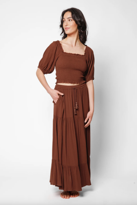 Woman wearing a brown top and long skirt set on a white background