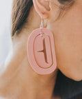 Close up of model wearing large ovoid earring with trigon cutout in antique peach color acrylic.