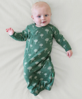 Baby wearing a green swaddle with tree pattern on a light background
