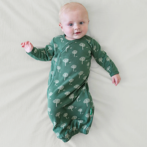 Baby wearing a green swaddle with tree pattern on a light background