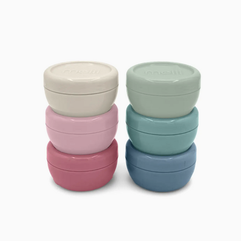 Two stacks of round, stackable storage containers with screw-on lids in pastel colors, photographed on a clean white background. The left stack contains cream, light pink, and dusty rose containers, while the right stack contains mint green, teal, and slate blue containers.