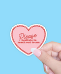 Heart-shaped sticker with text held by a hand against a blue background