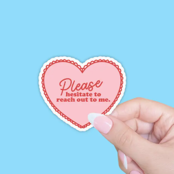 Heart-shaped sticker with text held by a hand against a blue background