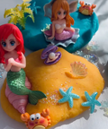 Mermaid figurines on a yellow base with starfish and other sea-themed decorations.
