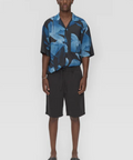 Person wearing a blue and black patterned shirt with black shorts on a white background