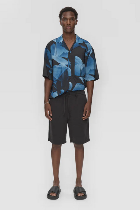 Person wearing a blue and black patterned shirt with black shorts on a white background