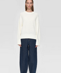 Person wearing a white sweater and dark blue pants on a white background