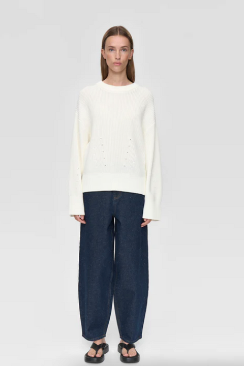 Person wearing a white sweater and dark blue pants on a white background