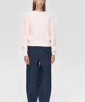 Woman wearing a light pink sweater and dark blue jeans on a white background