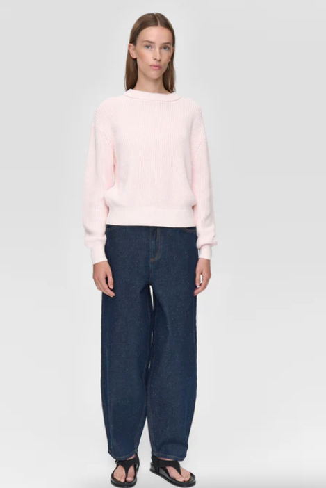 Woman wearing a light pink sweater and dark blue jeans on a white background