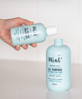 Person holding a bottle of Mint brand all-purpose cleaner with another bottle on a light background