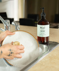 Person washing a dish in a sink with a bottle of dish soap on a counter.