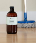 Bottle of floor wash on a wooden surface with cleaning tools in the background
