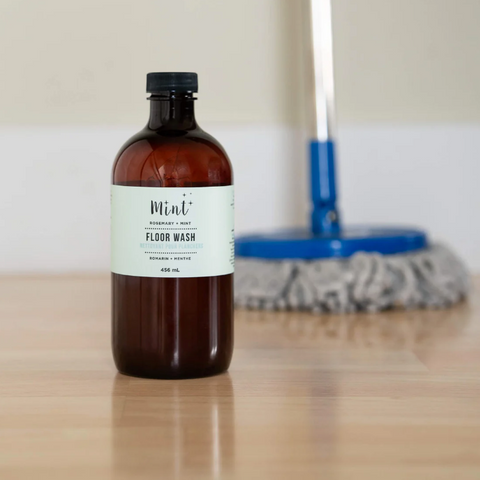 Bottle of floor wash on a wooden surface with cleaning tools in the background