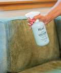 Hand holding a bottle of Miwai glass cleaner over a green couch.