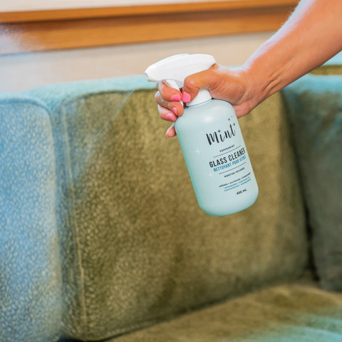 Hand holding a bottle of Miwai glass cleaner over a green couch.