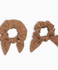 Two brown scrunchies with bow details on a white background