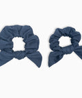 Two blue scrunchies with bow designs on a white background