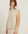 Woman wearing a beige knitted vest against a plain background