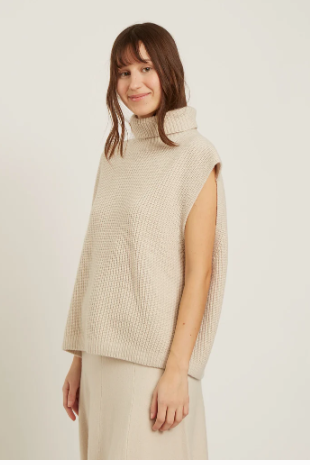 Woman wearing a beige knitted vest against a plain background
