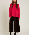 Person wearing a bright pink sweater and black pants on a white background