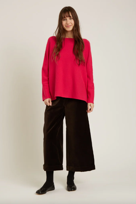 Person wearing a bright pink sweater and black pants on a white background