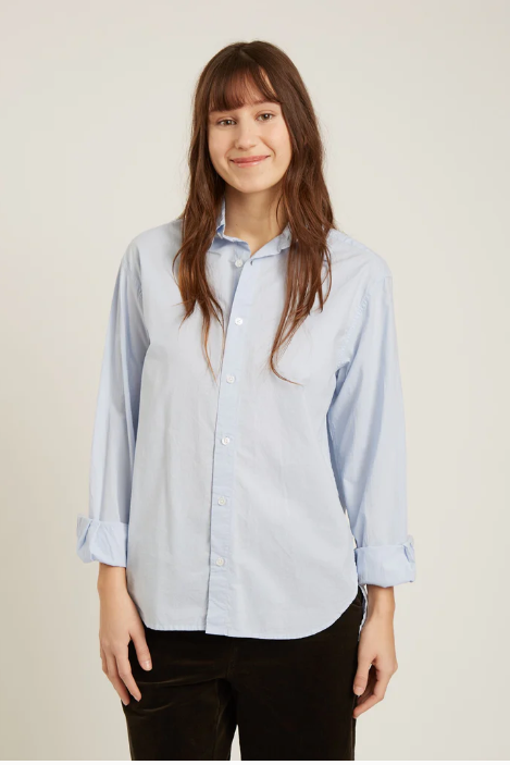 Woman wearing a light blue button-up shirt against a plain background