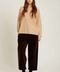 Woman wearing a beige sweater and brown pants on a white background