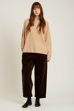 Woman wearing a beige sweater and brown pants on a white background