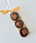 Chocolate-covered pecans in a clear cellophane bag with a gold ribbon on a white background
