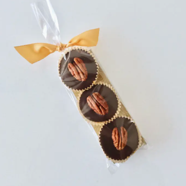 Chocolate-covered pecans in a clear cellophane bag with a gold ribbon on a white background