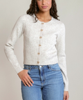 A woman modeling a cream ribbed knit cardigan with decorative star-shaped buttons, paired with blue jeans, against a solid light gray background.