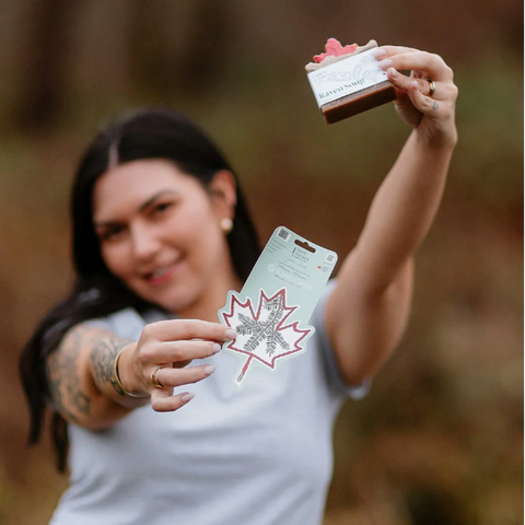 Person holding a soap bar and packaging with a maple leaf design outdoors
