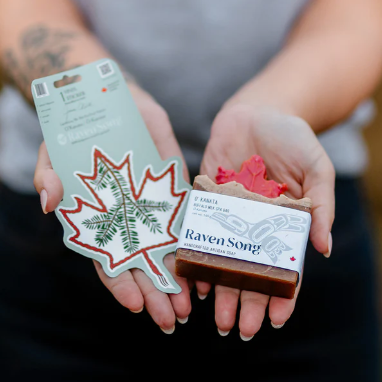 Person holding a bar of soap labeled 'Raven Song' and a branded leaf-shaped product.