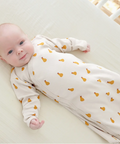 Baby wearing a white onesie with orange patterns, lying on a white surface.