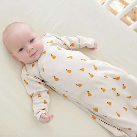 Baby wearing a white onesie with orange patterns, lying on a white surface.