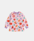 A pink long-sleeve art smock with an all-over colorful floral and leaf pattern, featuring purple cuffs and collar, displayed on a light gray background.