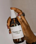 Hand holding a bottle labeled 'Peppercorn + Pine' against a neutral background