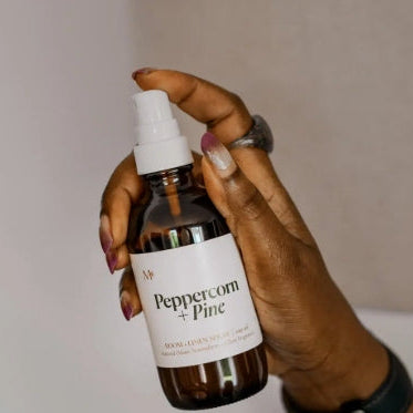 Hand holding a bottle labeled 'Peppercorn + Pine' against a neutral background