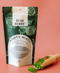 Bush Berry Mighty Minty package with a wooden scoop on a pink background